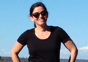 A young woman wearing a black t-shirt and sunglasses with blue sky as background.