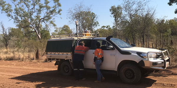 Two people standing next to a 4WD on a dirt road in the Australian bush.