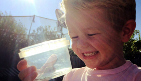 A smiling child with an insect in a container