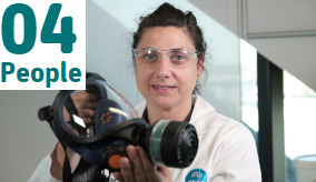 Researcher in lab coat holding a respirator mask.