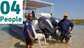 Two Indigenous rangers standing in the water near a boat