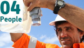 a man in a hard hat and orange hi vis top looks at a sample in a plastic container