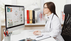 A doctor sitting at a computer with data graphs on the screen 