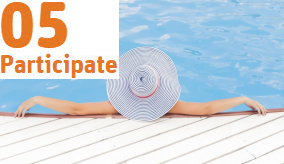 A woman wearing a large white and blue striped sun hat leaning against the edge of a swimming pool with her back to the camera
